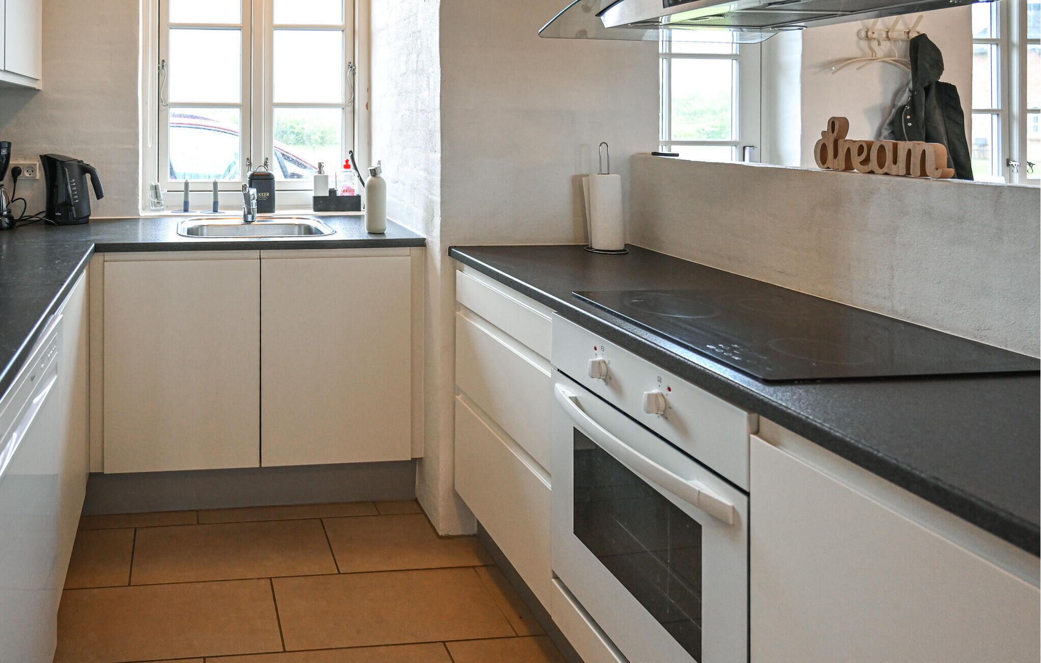 A compact kitchen with a black countertop, white cabinets, a built-in oven, and a window providing natural light.
