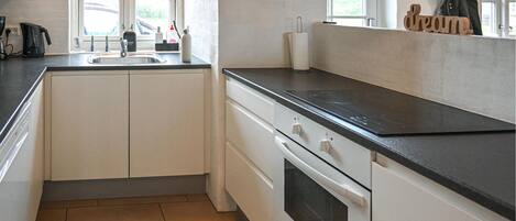 A compact kitchen with a black countertop, white cabinets, a built-in oven, and a window providing natural light.