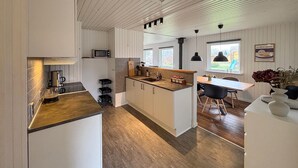A modern kitchen with a central island, a dining area with a table and chairs, and a view of the outdoors through large windows. - Cozy home in Sydals with sauna (Sydals)