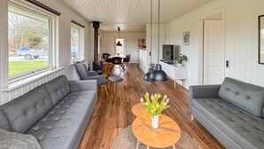 A spacious living room with two grey sofas, a wooden coffee table with a vase of flowers, a dining area with a table and chairs, and a TV on a white cabinet. - Cozy home in Sydals with sauna (Sydals)