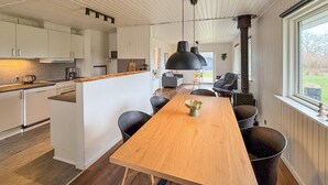 A modern kitchen with white cabinets, a wooden island, and a dining area with a long table and chairs. - Cozy home in Sydals with sauna (Sydals)