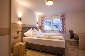A bedroom with a bed, bedside table, chair, and a window with curtains. - Apartment Zillertal Deluxe - Aparthotel **** AlpTirol (Kaltenbach)