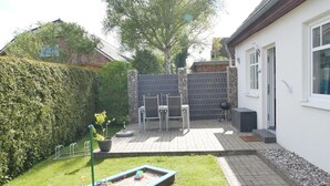 A backyard with a patio, a small boat with toys, a barbecue grill, and a stone wall. - Vacation home Sellin, child-friendly, barbecue, terrace, WLAN - Holiday home (Karlshagen)