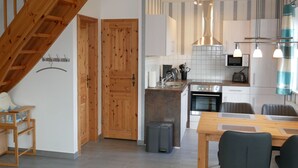 A modern kitchen with wooden accents, a dining area, and a staircase. - Vacation home Sellin, child-friendly, barbecue, terrace, WLAN - Holiday home (Karlshagen)