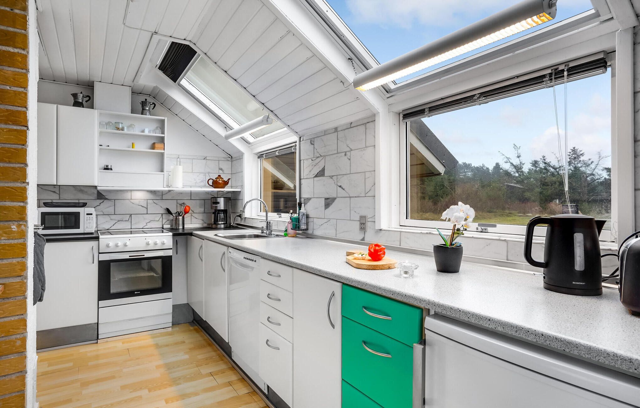 Une cuisine moderne avec des armoires blanches, un tiroir vert, un four à micro-ondes, une cuisinière et une fenêtre donnant sur des arbres.