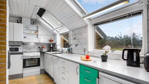 Une cuisine moderne avec des armoires blanches, un tiroir vert, un four à micro-ondes, une cuisinière et une fenêtre donnant sur des arbres.