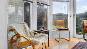 Une pièce moderne avec de grandes portes vitrées, un plancher en bois, un fauteuil moelleux, une chaise en osier et une petite table avec une bougie.