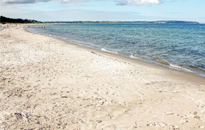 Une plage de sable avec des empreintes, une eau calme et une côte lointaine.