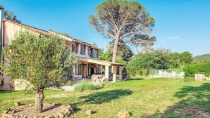 A two-story stone house with a covered patio, surrounded by a well-maintained lawn and trees. - Awesome home in Gonfaron (Gonfaron)