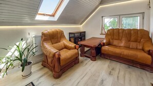 Um quarto com pé direito alto, um claraboia, poltronas de couro, uma pequena mesa de madeira e um radiador.