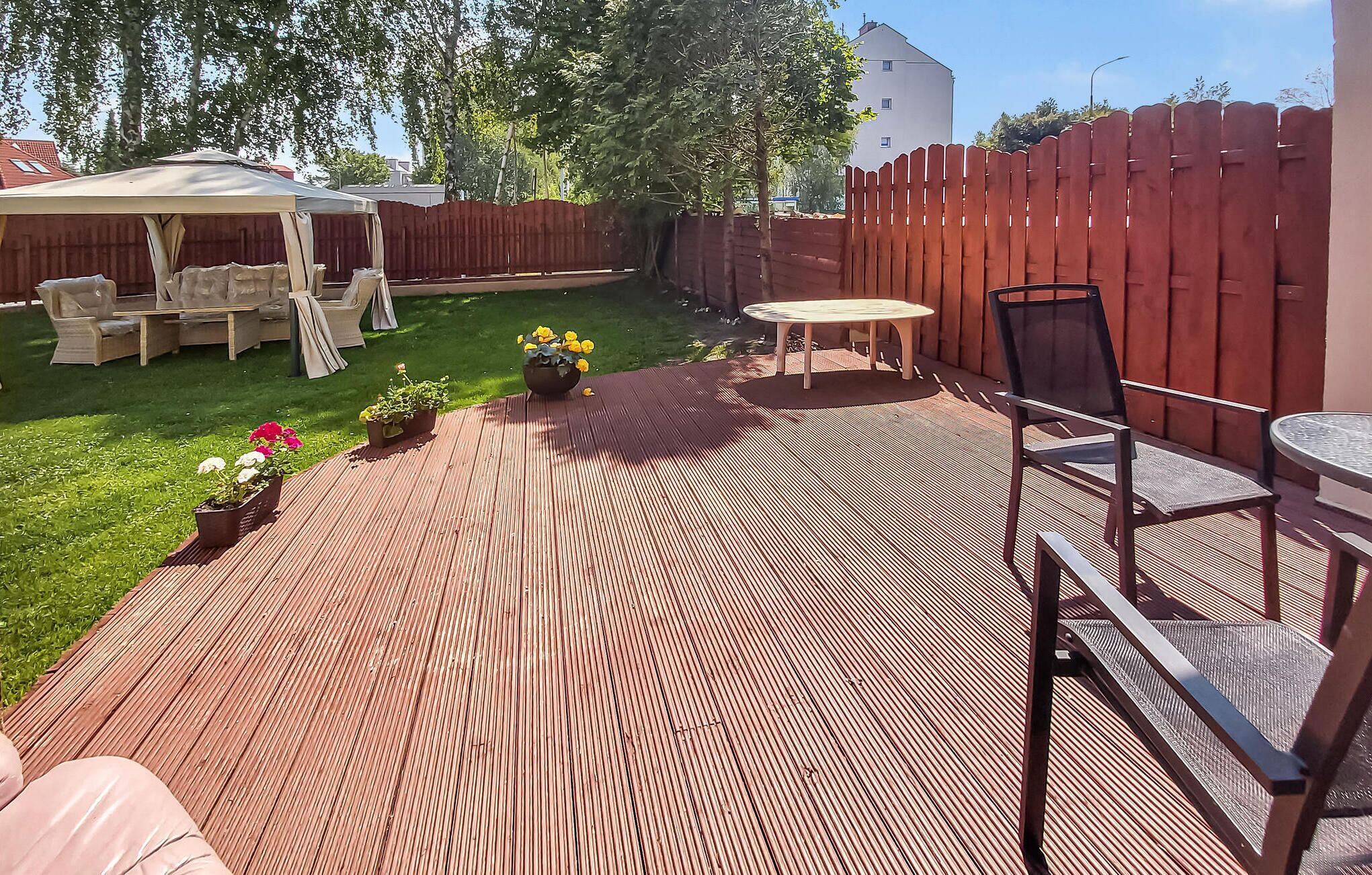 Un patio con cubierta de madera, mobiliario exterior y plantas en macetas.