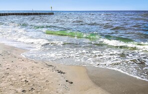 Ein sandiger Strand mit brechenden Wellen und einem Steg, der sich ins Wasser erstreckt.