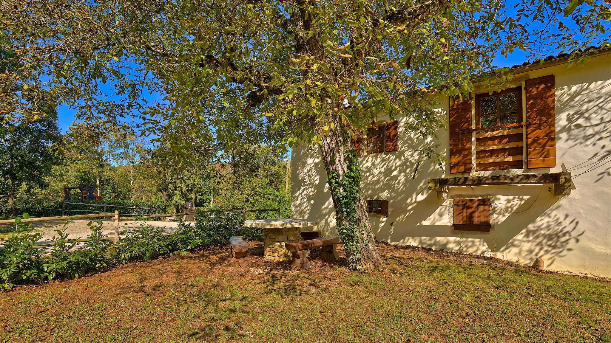 A rustic building with a stone fireplace, surrounded by a garden and trees.