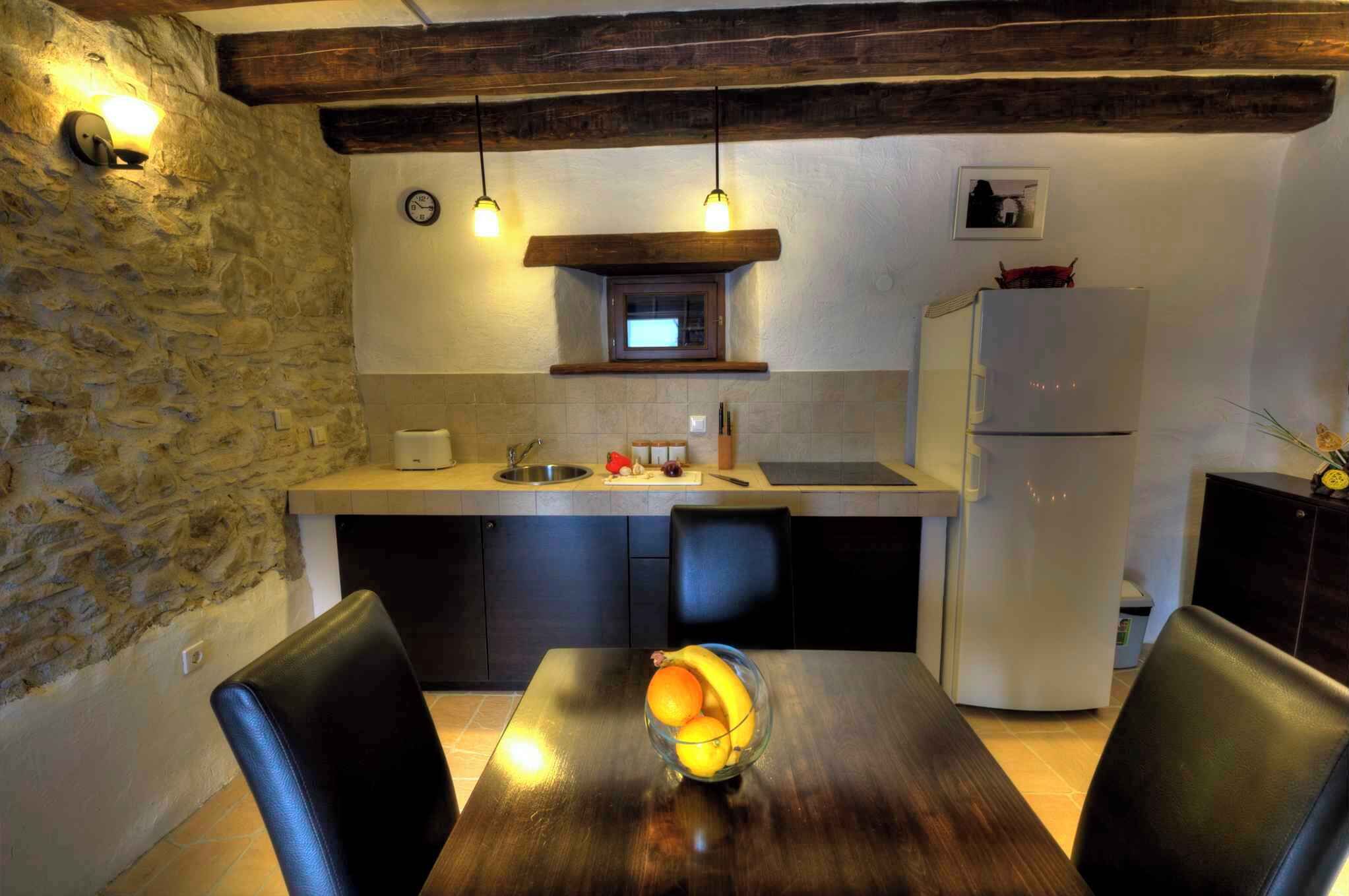 A compact kitchen with a stone wall, a wooden ceiling, a built-in microwave, a refrigerator, and a dining table with chairs.