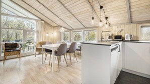 Eine moderne Küche mit Kochinsel, großen Fenstern und einem Essbereich mit Stühlen und Tisch.