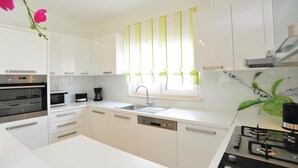 A modern kitchen with white cabinets, a built-in oven, a coffee maker, and a sink. - Amazing home in Pakostane (Pakostane)