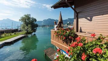Ein hölzernes Gebäude mit einem Balkon, der auf einen ruhigen Fluss mit viel Grün und Blumen blickt.