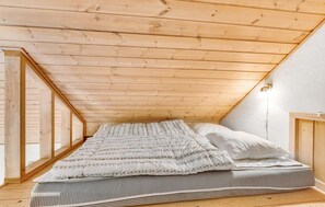 A bedroom with a sloped ceiling, wooden beams, a bed with a patterned duvet, and a bedside lamp. - Awesome home in Tarm with sauna (Tarm)