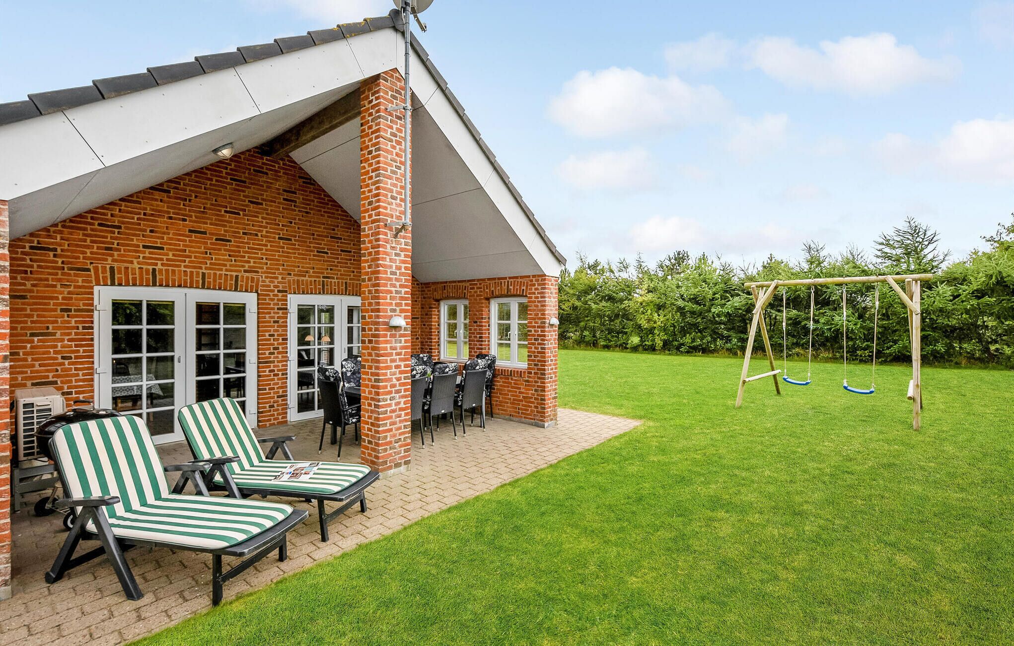 A brick house with a patio area featuring two striped lounge chairs and a table.