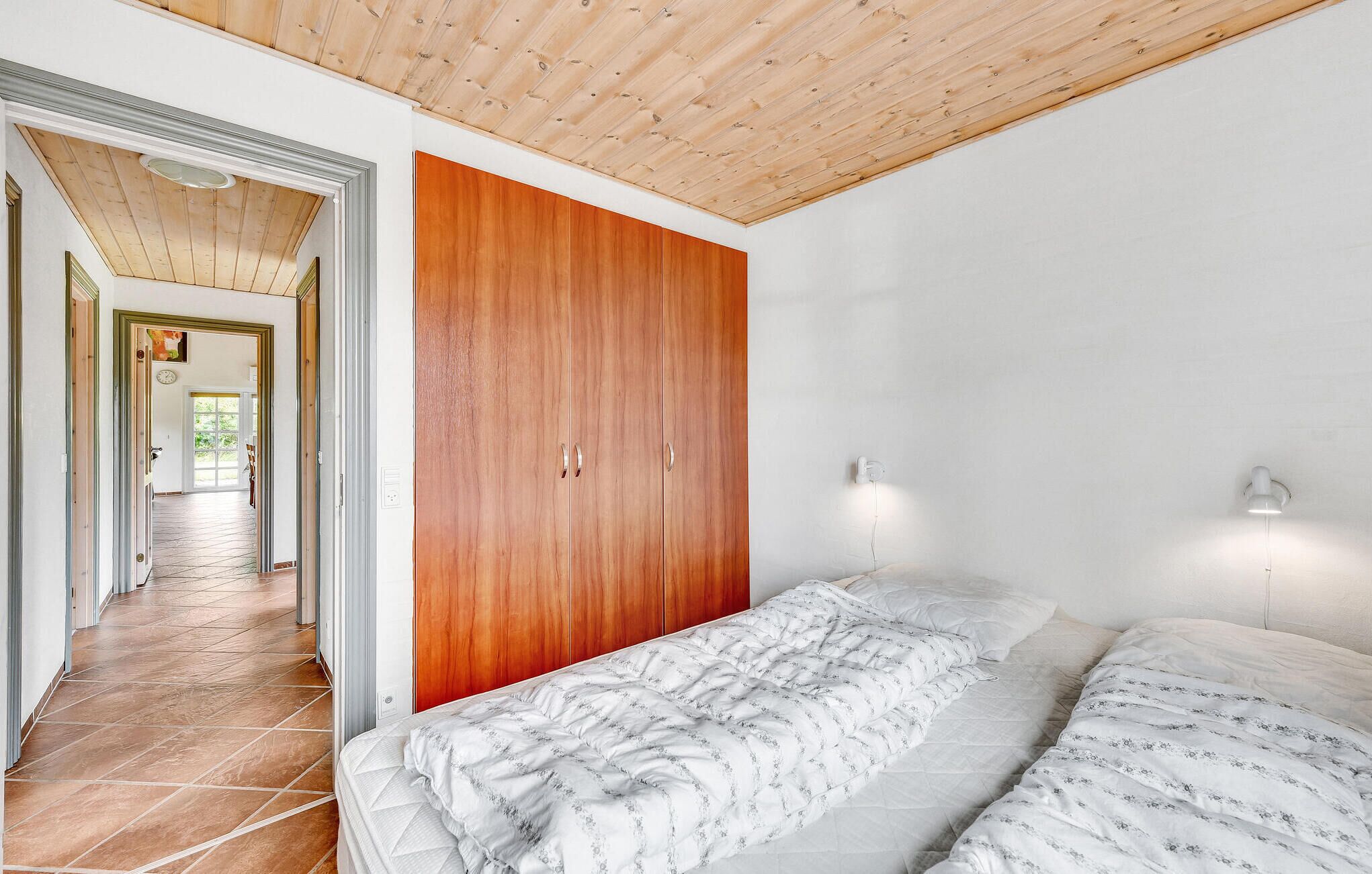 Une chambre avec une armoire en bois, un lit avec une literie à motifs et deux lampes fixées au mur.