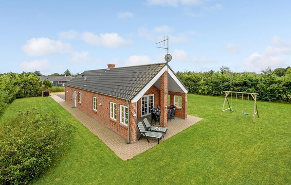 A brick house with a sloped roof, a satellite dish, and a patio with two chairs and a table. - Awesome home in Tarm with sauna (Tarm)
