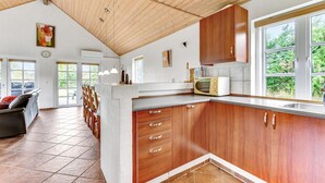 A spacious kitchen with wooden cabinets, a built-in microwave, and large windows offering a view of greenery. - Awesome home in Tarm with sauna (Tarm)