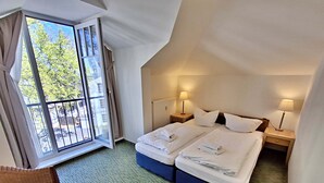 Ein Hotelzimmer mit zwei Betten, einem Fenster mit Vorhängen, einem kleinen Tisch und einem Sessel.