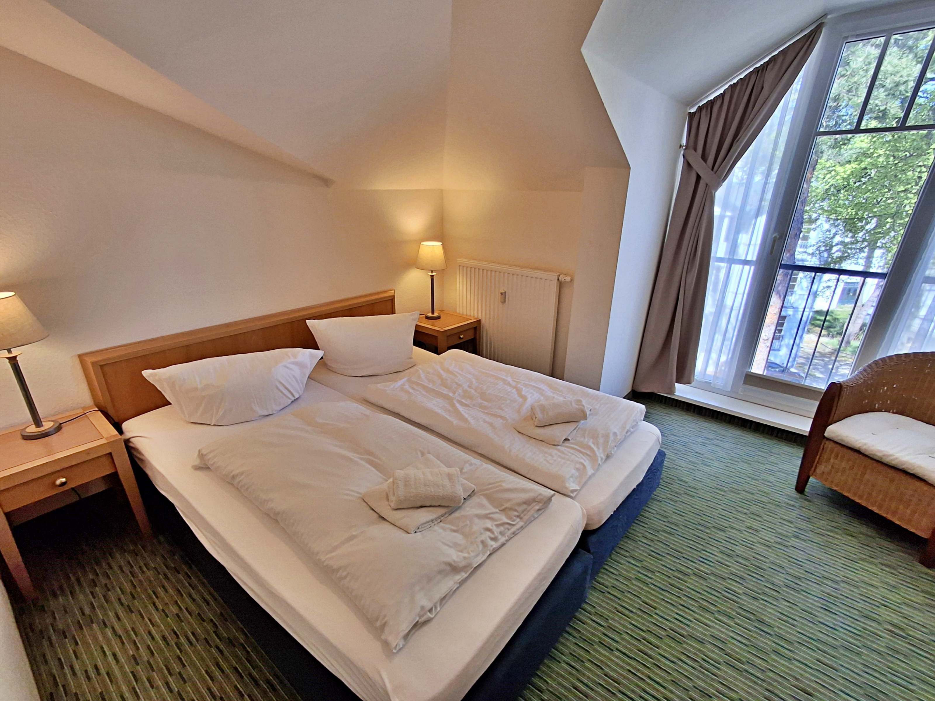 Hotellihuone, jossa on suuri sänky, kaksi yöpöytää, ikkuna verhoilla ja näkymä vehreään maisemaan.