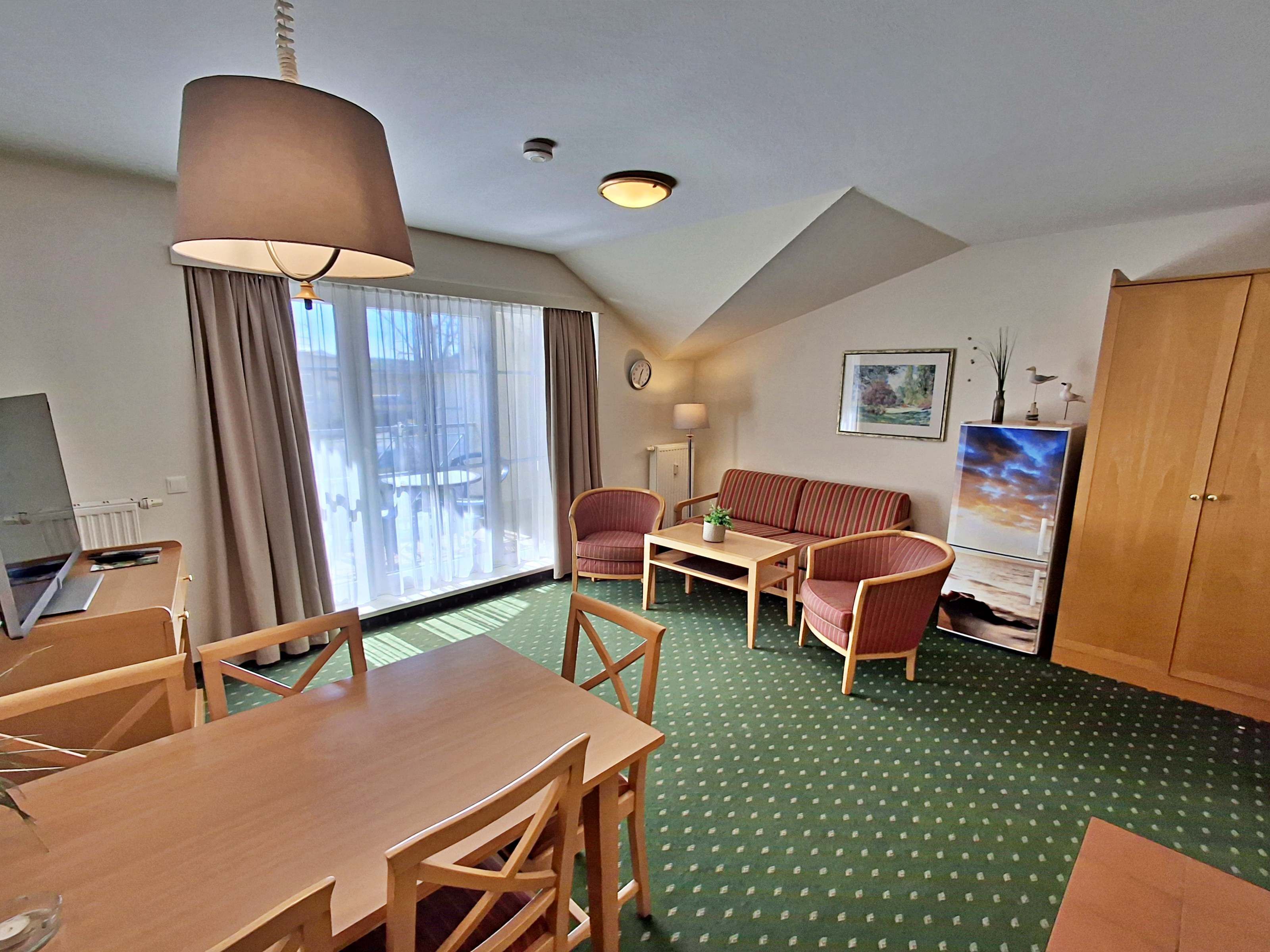 A hotel room with a dining table, chairs, a sofa, a TV, and a cabinet.