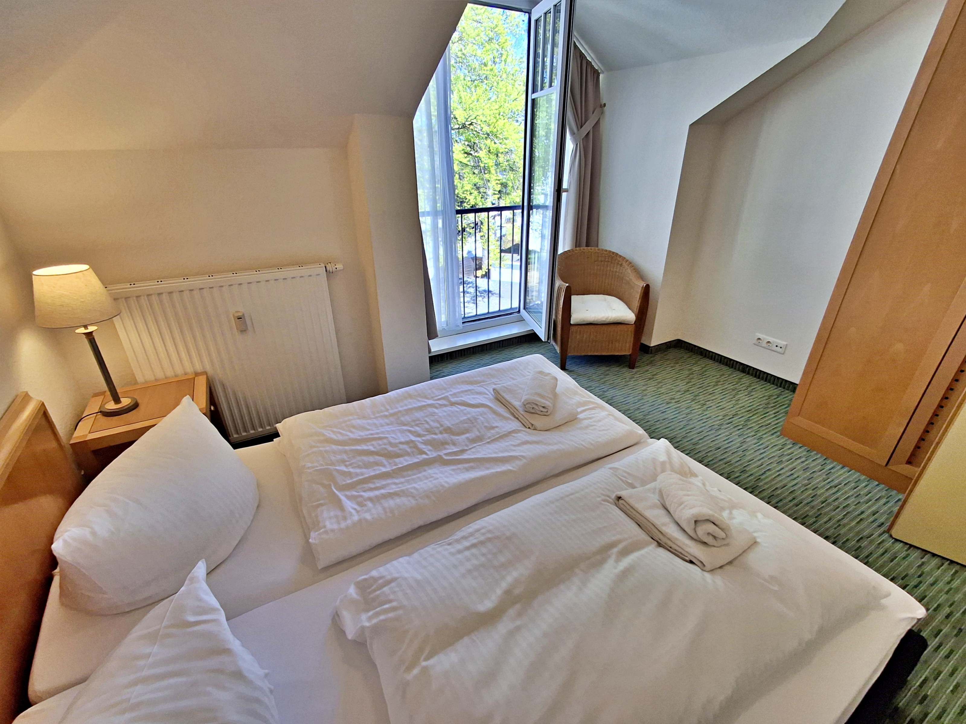 A hotel room with a bed, a chair, a lamp, and a window with a view of trees.