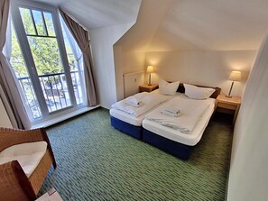 Une chambre d’hôtel avec deux lits, une fenêtre avec des rideaux, une chaise et deux lampes de chevet.