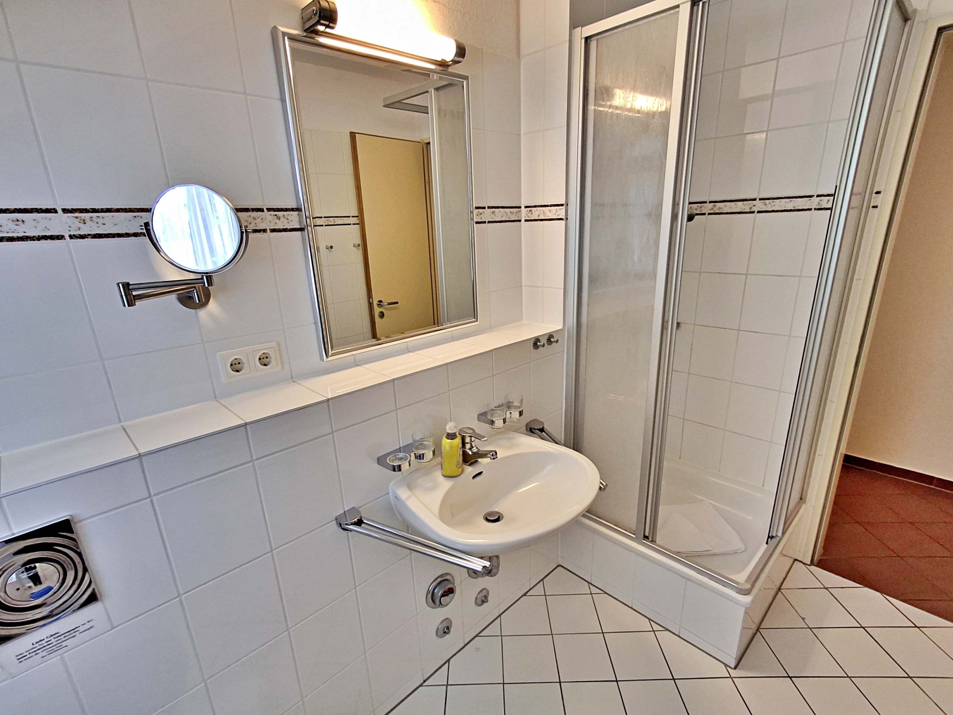 Ein Badezimmer mit einem weißen Waschbecken, einem Spiegel und einer Duschkabine aus Glas.