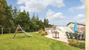 Ein Garten mit Rutsche, Gewächshaus, Sitzgelegenheit im Freien und einem Holzhaus.