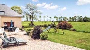 Eine Terrasse mit Gartenmöbeln, einer Schaukel und Blick auf ein gr ünes Feld.