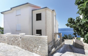 A two-story building with a stone facade, a balcony with a table and chairs, and a view of the sea.