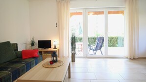 Una sala de estar con un sofá, un televisor, una mesa con una vela y vistas a un balcón con una silla.