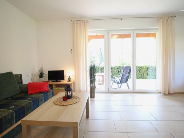 Un salon avec un canapé, un téléviseur, une table avec une bougie et une vue sur un balcon où se trouve une chaise.