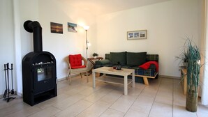 Una sala de estar con un estufa de madera negra, un sofá verde, una mesa de centro blanca y una silla roja.