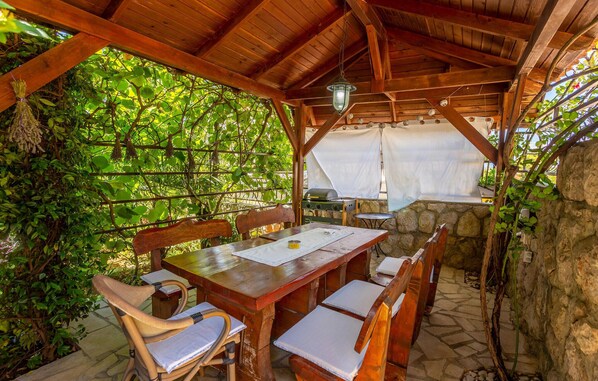 An outdoor wooden pergola with a table and chairs, surrounded by lush greenery. - Amazing apartment in Omisalj with WiFi (Omisalj)