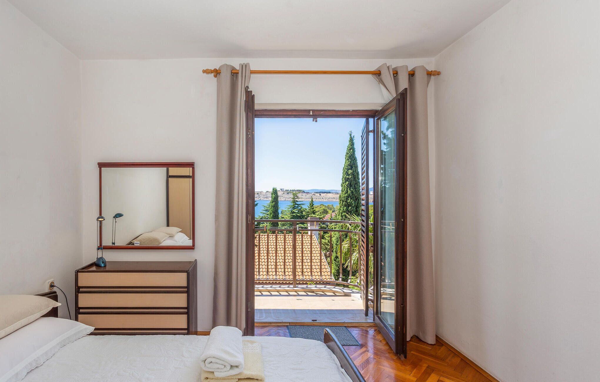 Ein Schlafzimmer mit Bett, Kommode, Spiegel und einem Balkon mit Meerblick.