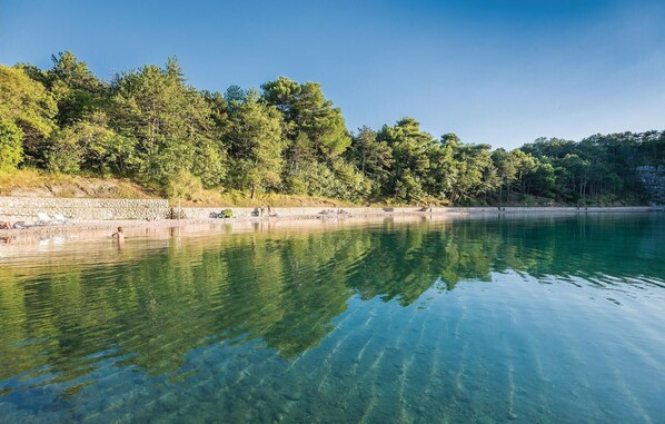 A clear lake with a stone wall and trees along the shore. - Beautiful apartment in Omisalj with house sea view (Omisalj)