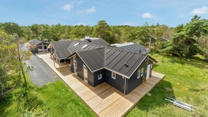 Ein modernes, blockhausähnliches Gebäude mit mehreren Zimmern, einer Holterrasse und einer umliegenden bewaldeten Gegend.