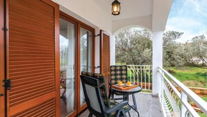 Un balcón con una mesa y sillas, vista a árboles y una puerta de madera.