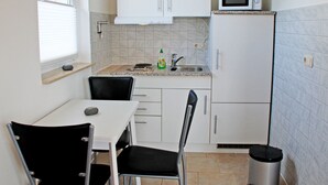Une cuisine de taille réduite, avec des meubles blancs, un four à micro-ondes, un évier et une poubelle.
