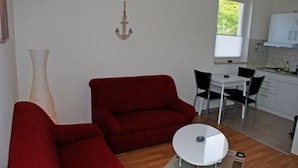 Un espace de vie compact comprenant un canapé rouge, une petite table ronde et un coin repas avec des chaises.