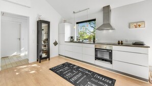 A modern kitchen with white cabinetry, a stainless steel range hood, and a window with a view of trees. - Beautiful home in Skjern with sauna (Skjern)