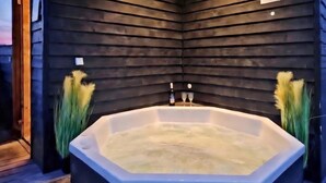 A corner room with a large octagonal bathtub, dark wooden walls, and two tall, green plants. - Beautiful home in Skjern with sauna (Skjern)