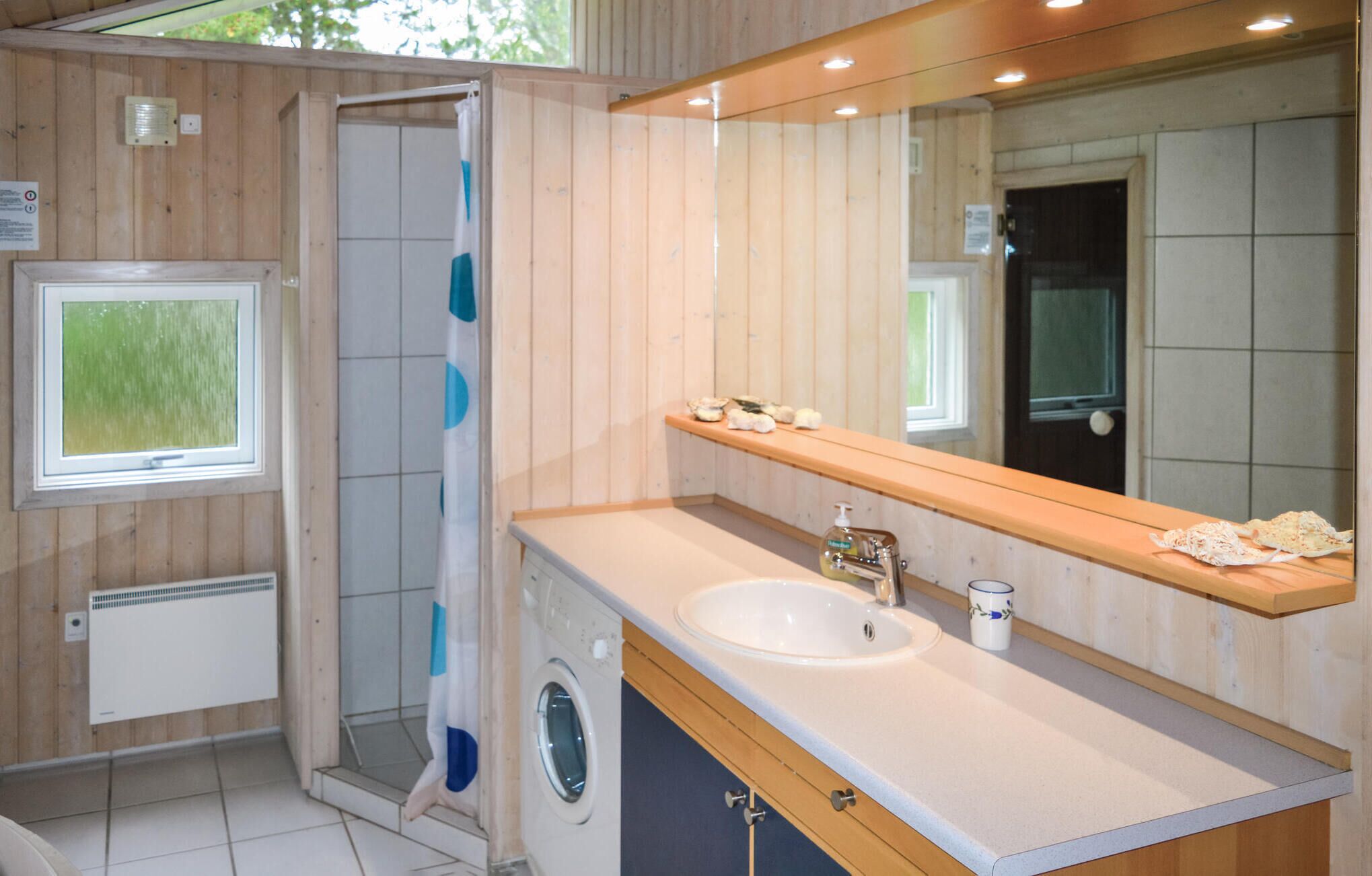 A modern bathroom with a built-in shower, a large mirror, a sink, and a small shelf with toiletries.