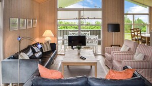 Una sala de estar moderna con un sofá de cuero negro, sillones a rayas, una mesa de centro de madera y un televisor.
