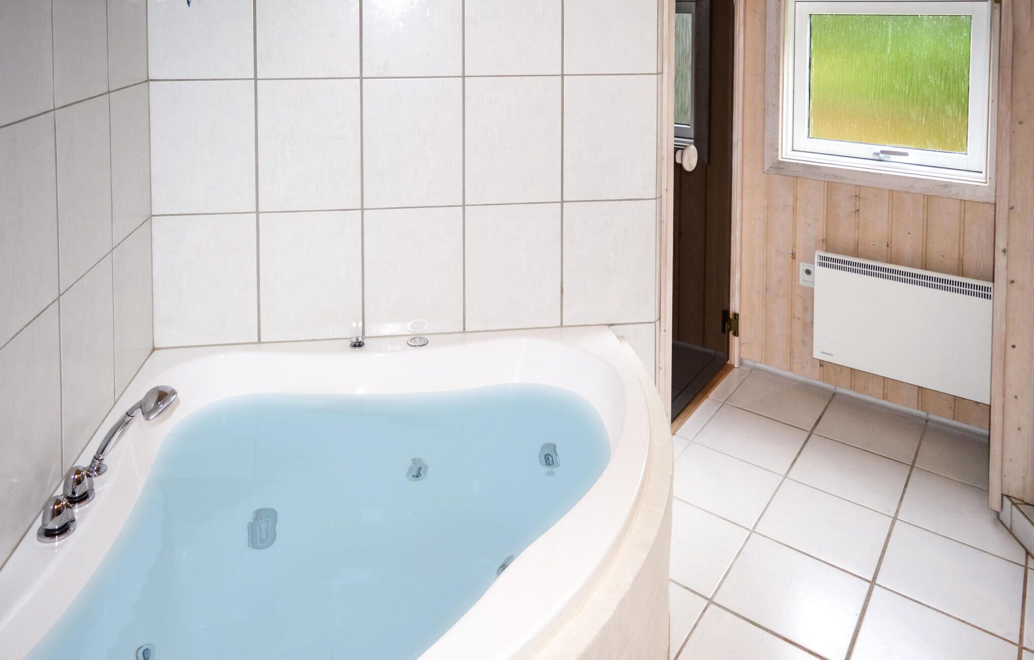 A bathroom with a bathtub, tiled walls, a window, and a radiator.